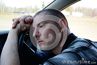 A sad young man is sitting in the car, leaning on the steering wheel. Stock Photo