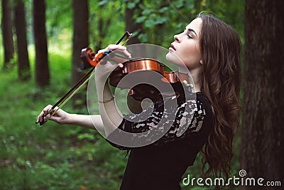 Sad young woman enthusiastically playing the violin romantic work in the Park among the trees Stock Photo