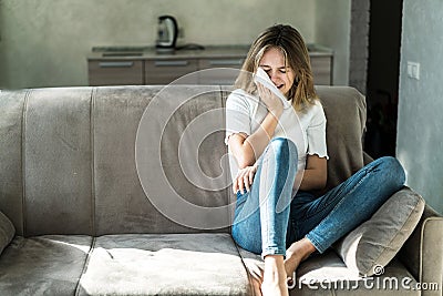 Sad young woman sitting on the couch at home and crying Stock Photo