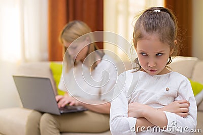 Sadness young girl. Portrait of bored daughter with mother using cellphone on sofa. Stock Photo