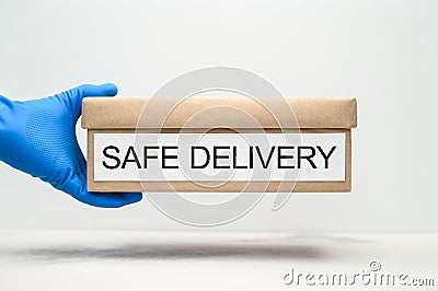 Safe delivery of packages at home during the coronavirus pandemic. A hand in a blue medical glove holds a cardboard box Stock Photo