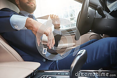 Safe driving. Cropped image of young businessman in formal wear is fastening the seat belt while sitting in his car Stock Photo