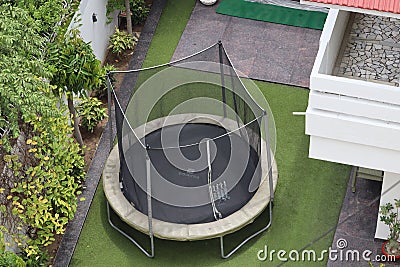 A safe trampoline is kept in the green garden. Kids like to jump on elastic circular rubber kept at home. Stock Photo