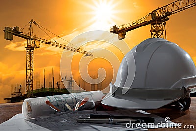 safety helmet and architect pland on wood table with sunset scene and building construction Stock Photo