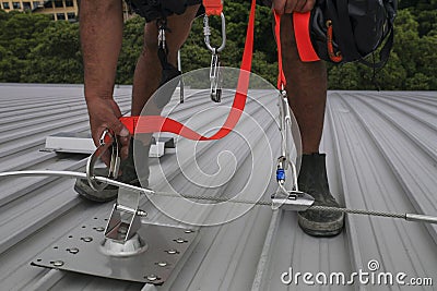 Trained worker clipping stainless industrial locking hook into fall arrest roof anchor point systems Stock Photo
