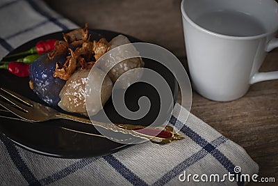 Sago pork in circle black plate with fried garlic toping have white cup place backside and gold fork place on black plate and Stock Photo