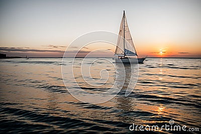 A sailboat bobbing on the horizon at sunset Stock Photo