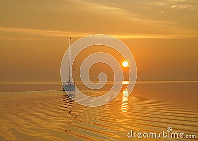 A sailboat departs a quiet anchorage into a bright yellow sunrise Stock Photo