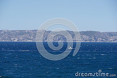 Sailboat gliding across a sparkling blue sea with mountains and a blue sky in the background Stock Photo