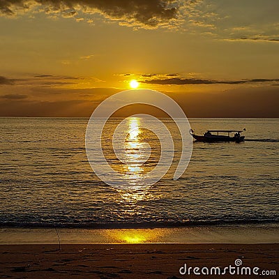 Sailboat gliding across a tranquil ocean during the golden hour of sunset in Lombok, Indonesia Stock Photo