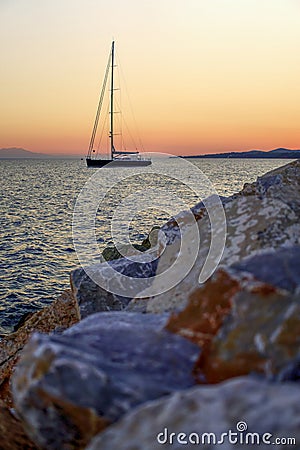 Sailboat on the sea at sunset, rocks in foreground Stock Photo