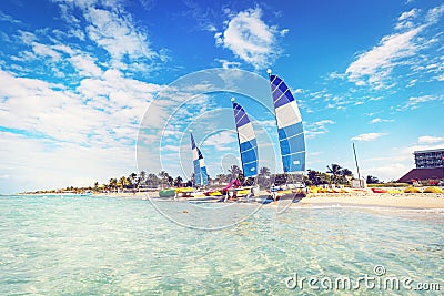 many tourist boats, kayaks and catamarans stand on the shore against the backdrop of a tropical island. Sailboats anchored in Stock Photo