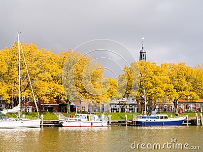 Sailboats at jetty in marina, trees in autumn colours and storm clouds, Enkhuizen, Netherlands Editorial Stock Photo