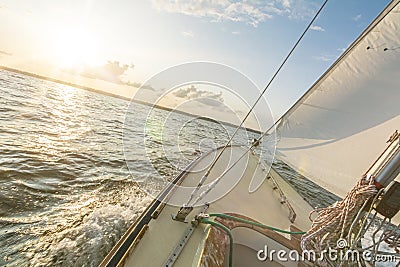 Sailing boat sailing fast into the beautiful sunset during choppy sea with tilted horizon Stock Photo