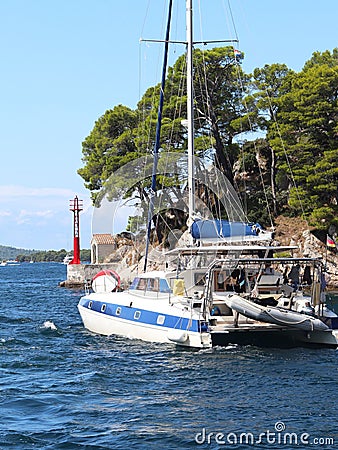 Sailing catamaran sails along the rocky green coast past the red literary sign - the fairway lighthouse. City of Sibenik in the Da Editorial Stock Photo