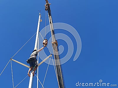 A sailor climbing up to fix the sail boat mast in Kudat, Malaysia. Stock Photo