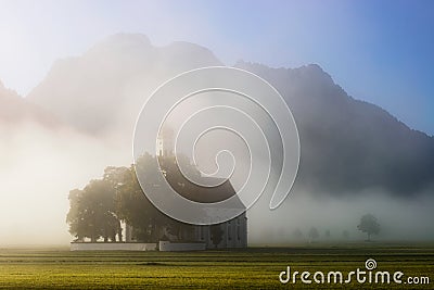 Saint Coloman church with warm light shining through the fog near Neuschwanstein Castle, Fussen, Bavaria, Germany Stock Photo