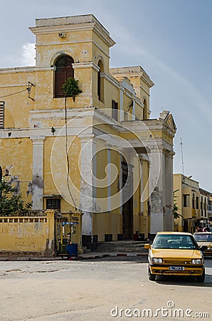 Saint-Louis, Senegal - October 14, 2013: Fading yellow colonial building and street with taxi in town of St. Louis Editorial Stock Photo