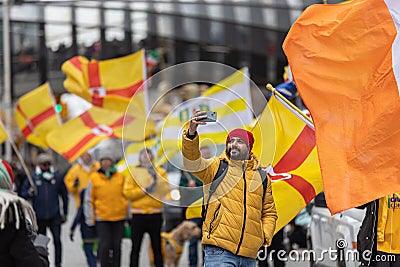 Saint Patrick's Day parade with a man taking a selfie in front of a group marching with County Antrim flags Editorial Stock Photo