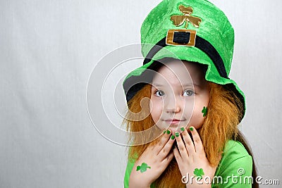 Saint Patricks Day celebration. Nice pensive little girl with decorative red beard, green shamrok leaf on her cheek and leprechaun Stock Photo