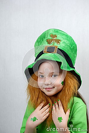 Saint Patricks Day. Endearing smiling small girl with decorative red beard, green shamrok leaf on her cheek and leprechaun hat, Stock Photo