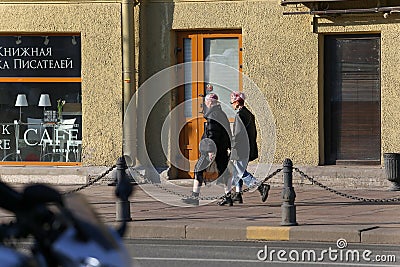 Two young fashionable girls walk along a street in the center of the city Editorial Stock Photo