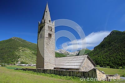 Sainte Cecile Church with Ceillac village, pine tree forests and mountain range covered with snow in the background, Stock Photo