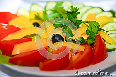 Salad of assorted vegetables in a plate stands on a festive table. Red tomatoes, cucumbers, olives, yellow pepper, parsley Stock Photo