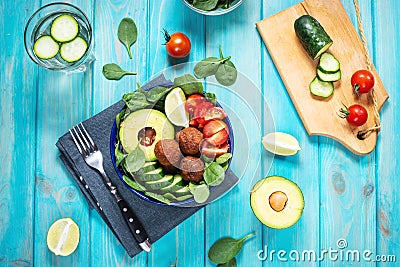 Salad with avocado, falafel, cucumber, cherry tomato and spinach on blue wooden background. Healthy vegan lunch bowl Stock Photo