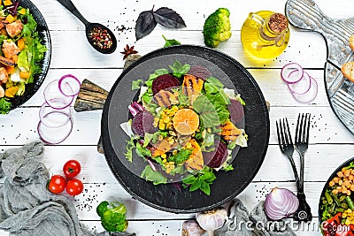 Salad: beetroot, pumpkin, corn and lettuce in a black plate on a white wooden background. Top view. Stock Photo