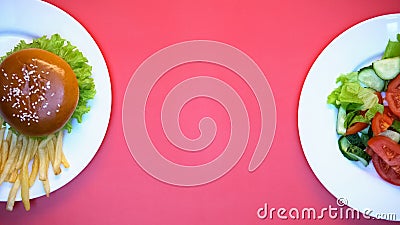 Salad, burger and french fries on white plates on pink background, fast food Stock Photo