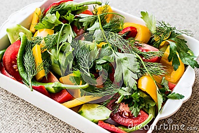 Salad with dill, yellow pepper, red pepper, parsley, tomato and cucumber in white bowl. Stock Photo