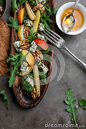 Salad with gorgonzola, rucola, pears, walnuts and honey in a long wooden plate. Stock Photo