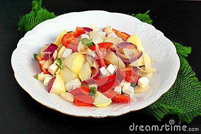 Salad with potatoes, red pepper, onion, basil and feta cheese on white plate on grey cloth on black background Stock Photo