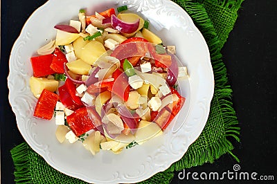 Salad with potatoes, red pepper, onion, basil and feta cheese on white plate on grey cloth on black background Stock Photo