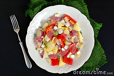 Salad with potatoes, red pepper, onion, basil and feta cheese on white plate on grey cloth on black background Stock Photo