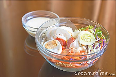 Salad in a transparent glass bowl with reflection; orange curtains background. Stock Photo