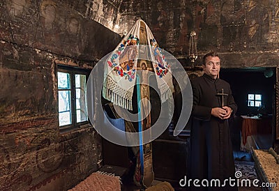 Salaj, Romania-May 16, 2018: Orthodox priest holding a Christian cross, praying in a old wooden church in Transylvania region, Editorial Stock Photo