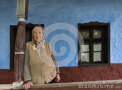 Salaj, Transylvania, Romania-May 15, 2018: old local woman in front of a rustic blue clay house in the rural countryside Editorial Stock Photo