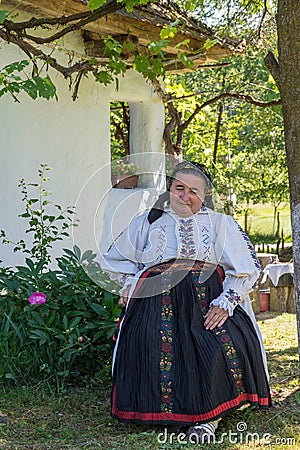 Salaj, Transylvania, Romania-May 14, 2018: old woman in traditional Romanian folk costume sitting in the garden in front of her Editorial Stock Photo