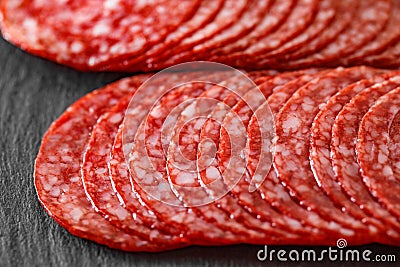 Salami sausage meat with bacon cut into circles in two rows close-up on slate stone plate, dark background, side view, selective Stock Photo