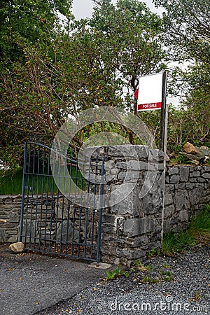 For sale blank sign at a gate of a property on an old stone fence. Real estate business. Mature property on the market to purchase Stock Photo