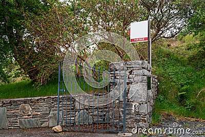 For sale blank sign at a gate of a property on an old stone fence. Real estate business. Mature property on the market to purchase Stock Photo