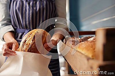 Sales Assistant In Bakery Putting Freshly Baked Organic Sourdough Bread Loaf Into Sustainable Paper Bag Stock Photo