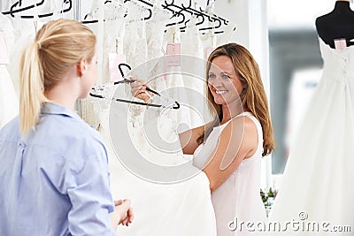 Sales Assistant In Bridal Store Helping Bride To Choose Wedding Stock Photo