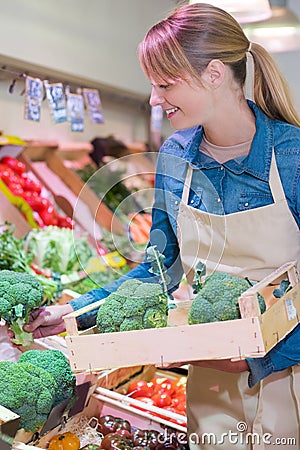 Sales assistant restocking broccoli in green grocers Stock Photo