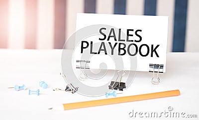SALES PLAYBOOK sign on paper on white desk with office tools. Blue and white background Stock Photo