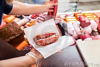 Sales woman in butchery holding sausage wrapped in paper Stock Photo