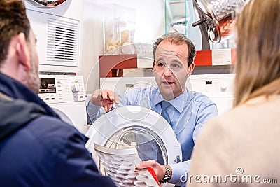 Salesman Explaining Product To Couple In Hypermarket Stock Photo