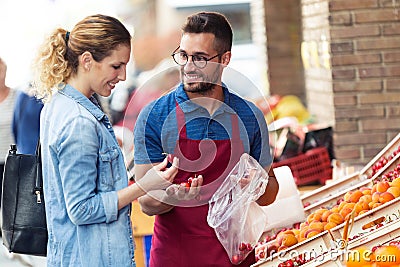 Salesman helping customer to choose some types of fruits in health grocery shop. Stock Photo